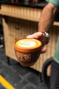 una persona che tiene una tazza di caffè con un leone sopra di Black Llama Hostel Cusco a Cuzco Altre 37 foto