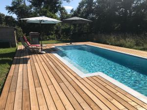 a swimming pool with a wooden deck and two umbrellas at La maison de Laujol in Moissac