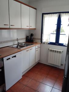 a kitchen with white cabinets and a sink and a window at La Casina Azul de May in San Juan de la Arena