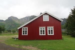 Una casa roja con ventanas blancas en un campo con montañas. en Lillehuset, en Kabelvåg