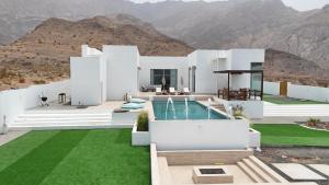 a white house with a pool and mountains in the background at Sea villa sifah in Muscat