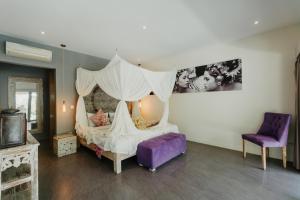 a bedroom with a canopy bed and a purple chair at Maylie Bali Villa & Bungalows in Canggu