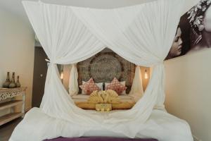 a bedroom with a canopy bed with white drapes at Maylie Bali Villa & Bungalows in Canggu