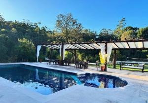 a swimming pool with a pavilion and a table and chairs at Chalé Estância do Coruja in Salesópolis