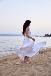 a woman in a white dress walking on the beach at Princess Resort, Santikos Collection in Agia Paraskevi