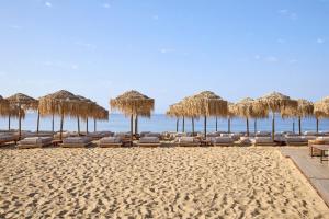 - une plage avec des chaises et des parasols en paille et l'océan dans l'établissement Princess Resort, Santikos Collection, à Agia Paraskevi