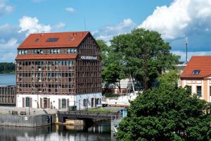 a building with a red roof next to a river at Old Mill Hotel in Klaipėda