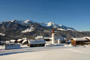 a snow covered village with a church in the mountains at Gasthof Hirschen in Sibratsgfäll