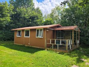 a small cabin with a porch in the grass at Camping les Hirondelles in Bourg-Sainte-Marie