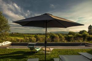 a black umbrella sitting in the grass with two chairs at Borgo Elissa Country Relais in Certaldo