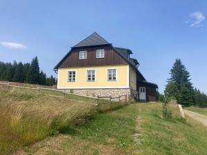 una casa gialla con tetto marrone su un campo di Apartmán Nad Modravou a Modrava