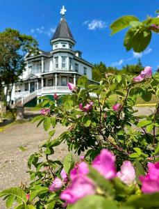 a large white house with a tower and pink flowers at Le Manoir du Vieux Presbytère in Port-Daniel