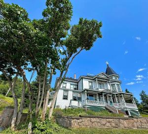 a large white house on a hill with trees at Le Manoir du Vieux Presbytère in Port-Daniel