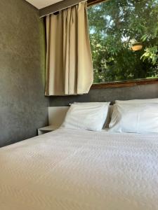 a bed with white pillows in a bedroom with a window at Yannai Chalé Praia in Ilhabela