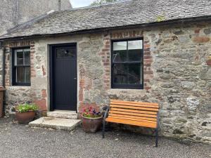 un banco de madera frente a un edificio con puerta en The Bothy at Christmas Cottage, en Rowardennan