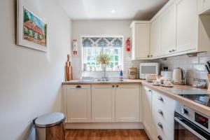 a white kitchen with a sink and a window at Beautiful Riverside Cottage with Large Garden, 2BR in Boldre +17 photos