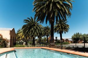 a swimming pool with palm trees and a fence at Tuileries at De Bortoli Rutherglen in Rutherglen
