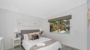 a white bedroom with a bed and a window at Casa Bianca - Pearl Beach in Pearl Beach