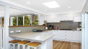 eine Küche mit weißen Schränken und einer Theke mit Stühlen in der Unterkunft Paradise - Pearl - Modern With Wifi in Pearl Beach