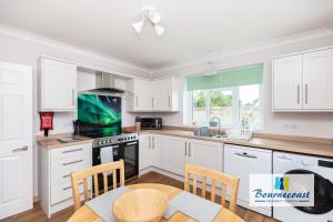 a kitchen with white cabinets and a table with a television at Bournecoast Family chalet bungalow - garden -9600 in Mudeford +50 photos