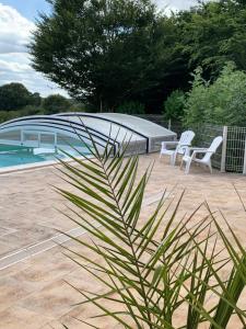 a patio with two white chairs and a swimming pool at Gite de Groupe Aux Instants Partagés in Fontenay-sur-Vègre