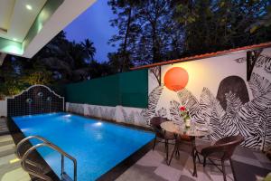 a pool with a table and chairs next to a wall at TreeHouse Nova in Cansaulim