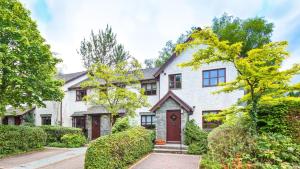 a white house with a red door and trees at 2 Bedroom Lake District Cottage At Windermere Marina Village in Bowness-on-Windermere