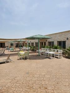 a patio with tables and chairs and an umbrella at ghroob farmhouse villa in Al Ḩamrānīyah