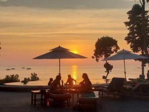 a group of people sitting under umbrellas at a beach at Dusit Buncha Koh Tao by Riya Group in Ko Tao