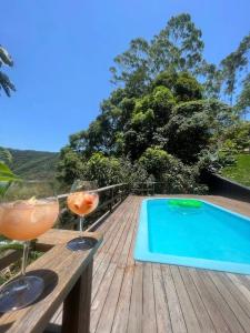 two wine glasses sitting on a wooden table next to a swimming pool at Casa Jasmim em Domingos Martins a 5km do Centro in Domingos Martins