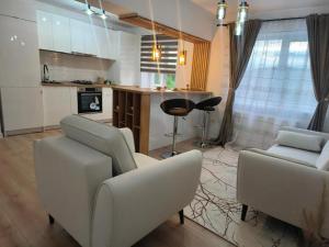 Una sala de estar con dos sillas blancas y una cocina. en Apartament Theodora, en Curtea de Argeş 11 fotos más