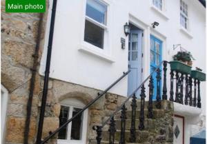 a white building with a blue door and a staircase at Cornish Cottage in Downalong, St Ives in St Ives