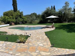 a swimming pool with an umbrella in a yard at The Retreat - Oak Lodge in Corfu