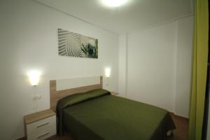 a small bedroom with a green bed and a lamp at Apartamentos Marina Playa de Torrevieja in Torrevieja