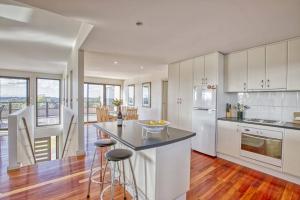 a kitchen with white cabinets and a island with bar stools at Georges Bay Luxury in St Helens
