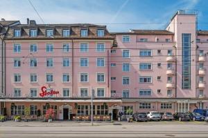 a large pink building with cars parked in a parking lot at Hotel Stoller in Zürich