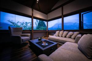 a living room with couches and a table and windows at Yufuin Kaze no Mori in Yufuin