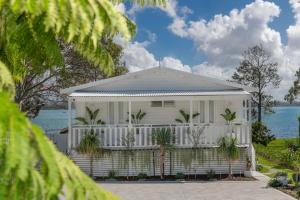 une maison blanche avec un porche et de l'eau en arrière-plan dans l'établissement The Cottage, à Bonnells Bay 3 autres photos