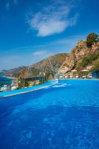 a swimming pool with blue water and a mountain at Baia Taormina - CDSHotels in Forza dʼAgro
