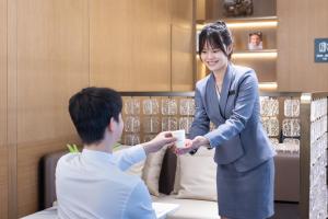 Una mujer le está entregando un teléfono celular a un hombre. en Atour Hotel Guangzhou Tianhe Sports Center - Free Shuttle bus to Canton Fair Hall & Free self-service laundry & Free midnight snack & near canton fair Purchaser certificate office & big shopping mall, en Guangzhou