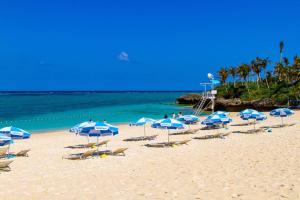 una spiaggia con molti ombrelloni e sedie blu e bianchi di 恩納村の飲食店多数 徒歩圏内のエリア 最大8名貸切 コンビニ徒歩30秒 ビーチまで徒歩3分 aコーディアルステイ1F a Fuzuchi