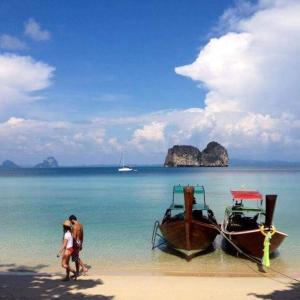 two people walking on a beach with two boats at Thanya Beach Resort - SHA Plus in Ko Ngai