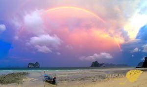 a rainbow over a beach with a boat on the sand at Thanya Beach Resort - SHA Plus in Ko Ngai