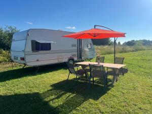 a rv parked in a field with a table and an umbrella at Countryside Relax in Liepupe