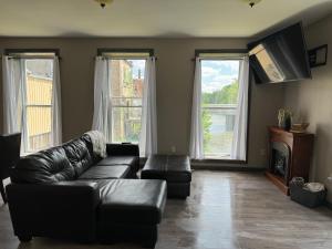 a living room with a black leather couch and two windows at Sugar on The Sugar River in Albany