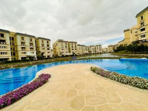 a large pool of water with buildings and purple flowers at Mountain View Hyde park luxury villa in New cairo