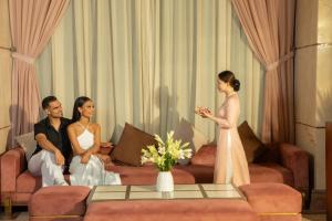 a bride and groom sitting on a couch with a woman in a white dress at Mandila Beach Hotel Danang in Danang