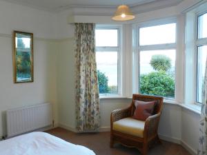 ein Schlafzimmer mit einem Stuhl und zwei Fenstern in der Unterkunft Ardbeag in Whiting Bay