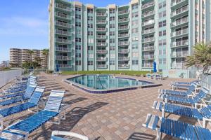 a pool with blue lounge chairs and a large building at Coronado Towers 703 in New Smyrna Beach