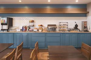 a kitchen with blue cabinets and wooden tables and chairs at Country Inn & Suites by Radisson, Michigan City, IN in Michigan City